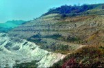 Počátkem 70. let 20. stol. byla v malém údolí u obce Dětaň na jižním okraji Doupovských hor vyhloubena jáma pro těžbu kaolinu, základní surovinu k výrobě porcelánu. Ložisko kaolinu (bílá hornina vlevo dole) je pokryto asi 50 m mocným souvrstvím sopečných popelů (tufů) a lávovým proudem  čedičové horniny těžené v malém lomu na vrcholu kopce (vpravo). Tufy tvoří  tzv. skrývku ložiska, která byla odtěžena v 7 etážích; tím byla vedle kaolinu  obnažena nejstarší fáze sopečné činnosti Doupovských hor, což umožnilo její paleontologický výzkum (obr. z r. 1974). Foto O. Fejfar
