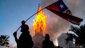 A demonstrator waves the Chilean flag outside of a burning church at dusk