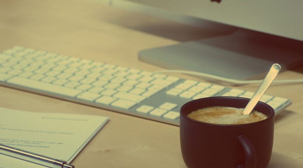 notebook with a pen and a cup of coffee in front of a computer screen